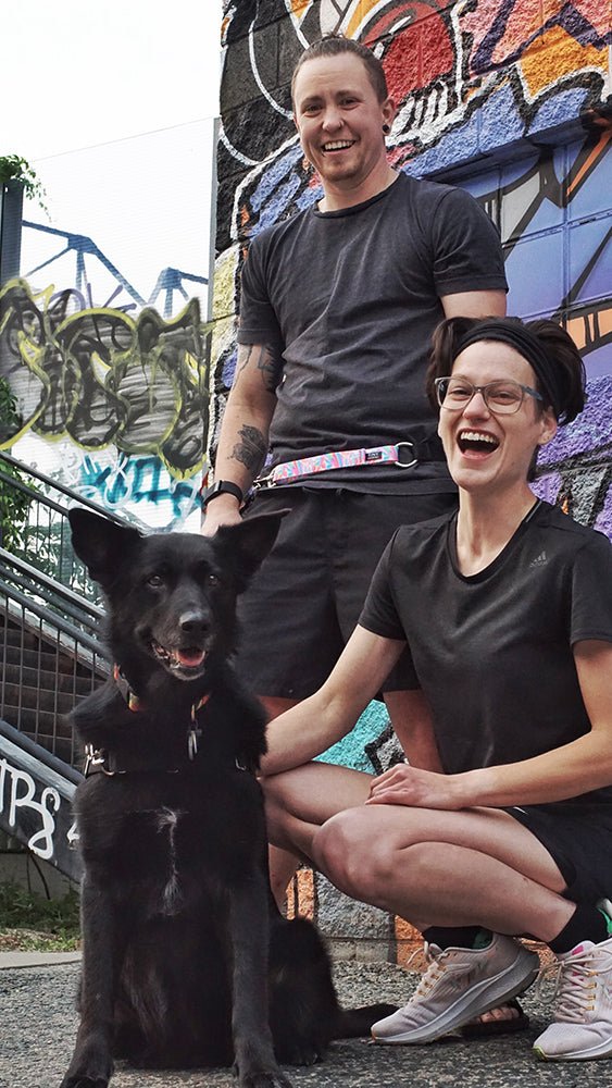 Two people posing with the 2023 Pride Leader and a seated black dog